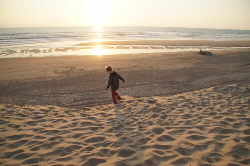 Un enfant joue sur une dune l'hiver avec le soleil qui descend vers l'horizon